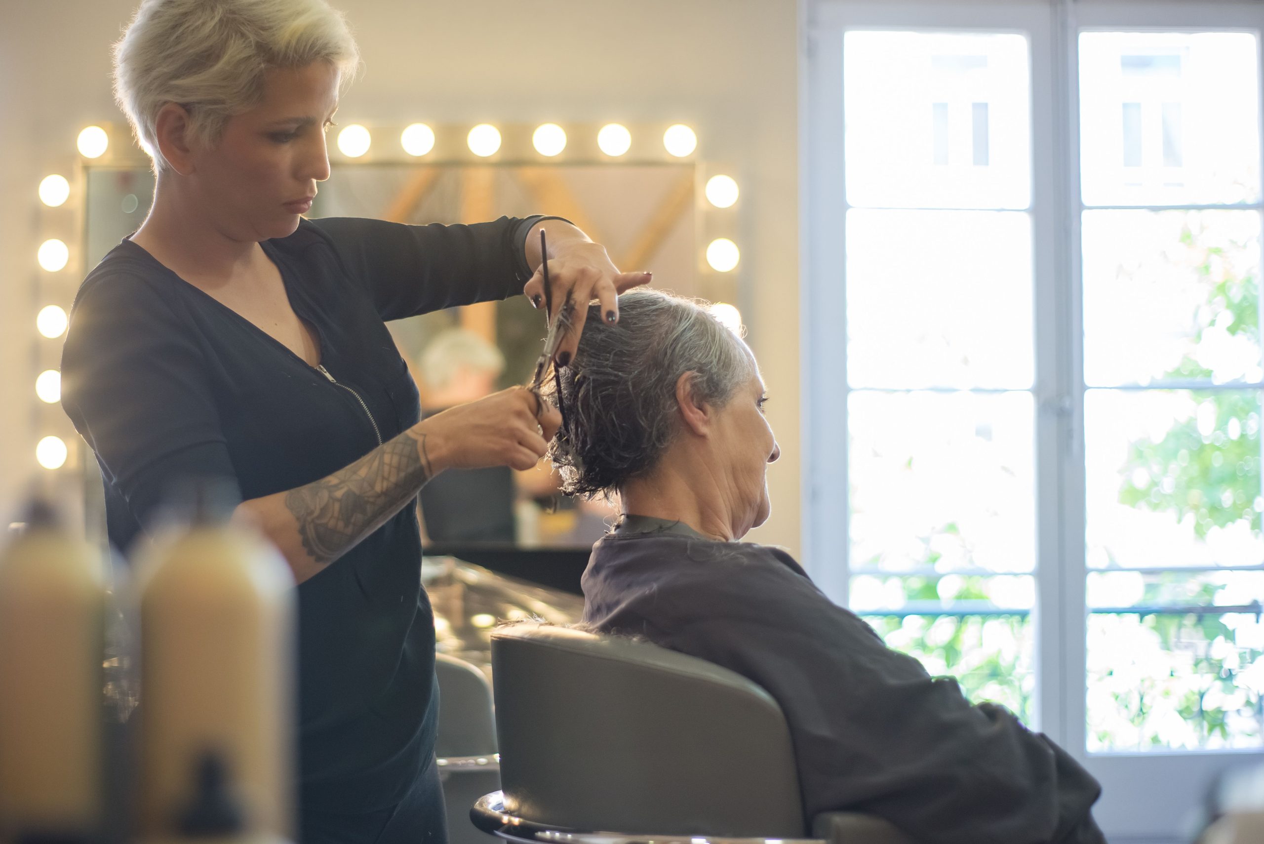 Friseurin stylt das Haar einer Kundin im hellen Salon